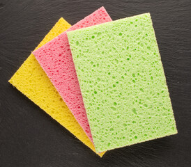 Three colored cellulose kitchen sponges on slate stone, macro, top view.