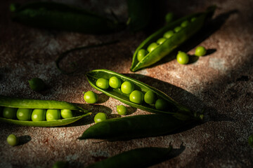 Fresh green peas in pods on stone surface in harsh sunlight.