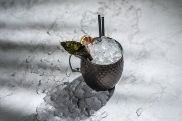 Cocktail in metal jar with ice and orange and nori garnish