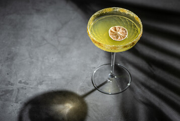 Yellow cocktail in martini glass with sugar garnish and dried orange tray marble background