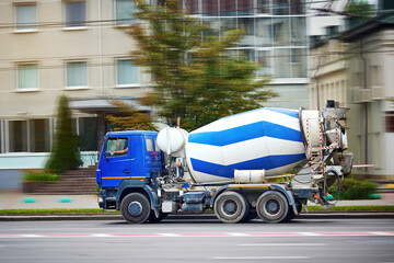 Mixer truck delivery ready concrete mixture on job site, delivering cement to construction site. Concrete mix truck rides to construction site, driving on city road. Cement truck with concrete - obrazy, fototapety, plakaty