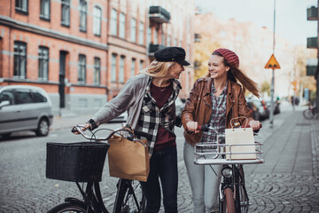 Obraz na płótnie Canvas Young women pushing their bicycles on a city street