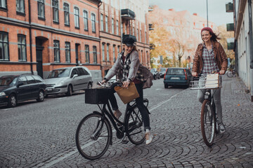 Two young women riding their bicycles on a city street