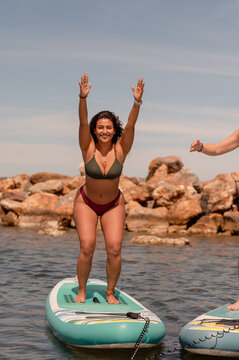 Cheerful woman with raised arms warrior 1 yoga pose on paddleboard