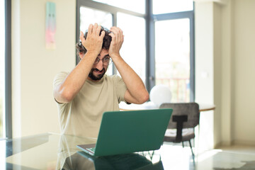 young adult bearded man with a laptop panicking over a forgotten deadline, feeling stressed, having...