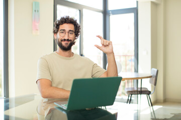young adult bearded man with a laptop holding an object ,showing, offering or advertising something small
