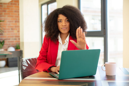pretty afro black woman looking serious showing open palm making stop gesture. businesswoman and laptop concept