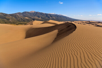 Fototapeta na wymiar Sand Waves - A panoramic Spring evening view of sand waves and rolling sand dunes, with Mt. Zwischen of Sangre de Cristo Range towering in background. Great Sand Dunes National Park & Preserve, CO, US