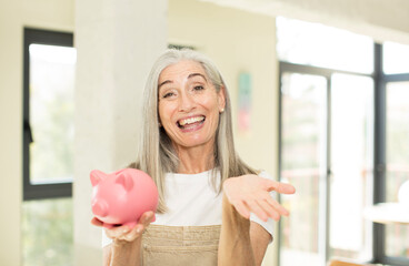 pretty senior woman smiling happily and offering or showing a concept. with a piggy bank