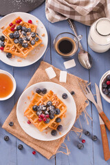 Waffles with red currant and blueberries on white dish.