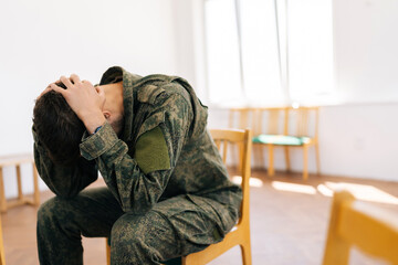 Side view of upset anxious veteran male in camouflage uniform with PTSD with head in hands, sharing trauma story sitting in circle during group therapy session. Concept of mental health, psychotherapy
