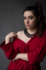 a beautiful young girl in a red shirt with a necklace with a handmade ornament on her neck is posing in a photo studio