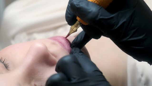 Permanent makeup procedure applying rose red pigment using tattoo machine in beautician salon. Microblading tattoo lips.