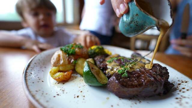 Food on plate person pouring sauce into red meat at restaurant