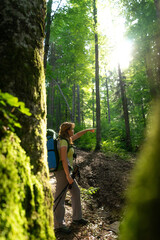 Naklejka na ściany i meble girl with backpack alone in green forest sunbeam with her hand hiking in the mountains tourism travel tourist hiking walks mental health rest recreation recovery in nature with nature active lifestyle