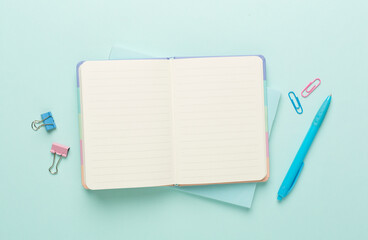 Open notebook with stationery on color background, top view