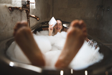 Obraz na płótnie Canvas beautiful sexy girl in a bubble bath reading a book, funny with big feet