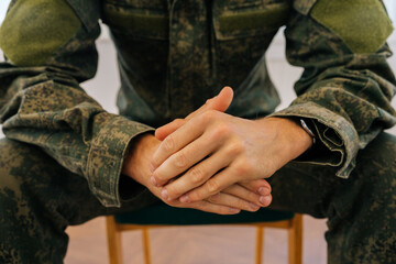 Closeup cropped shot of unrecognizable veteran male in camouflage uniform clenching hands sitting in circle during PTSD group therapy session. Concept of mental health, psychotherapy, social issues.