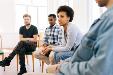 Side view of experienced african female psychologist telling group of people of different nationalities gathered for session about psychological practices. Concept of mental health, social issues