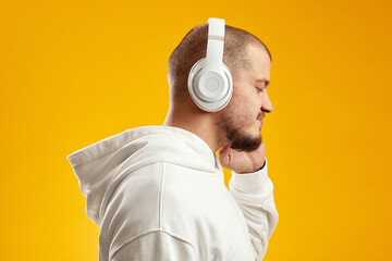 Side view of a cheerful young caucasian man listening to music with wireless headphones isolated...