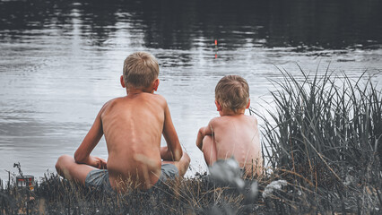 The boys are sitting on the river bank and fishing
