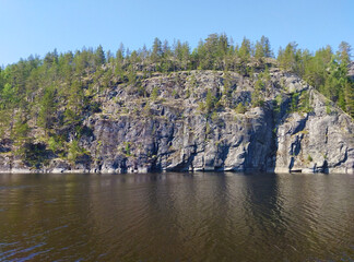 Rocky shore with large stones and trees reflected in calm water of northern lake. Beautiful summer nature of Ladoga lake. Karelia. Russia.