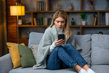 Obraz premium Sick woman wrapped in blanket with a high temperature calling on the phone. Photo of woman suffering cold and winter flu virus. Medical concept.