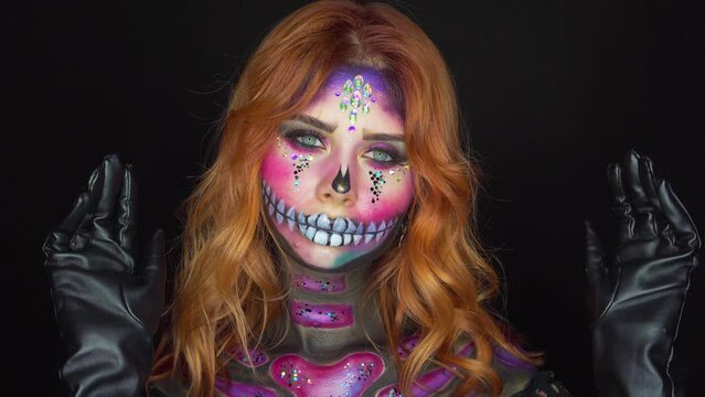 Beautiful woman with halloween professional make-up, girl sexy face sugar skull paints body art. Fashion model posing, red hair flying in wind, dark black mystical studio. party holiday sexy costume