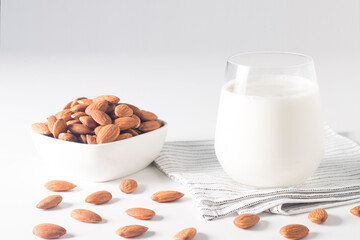 Organic almond milk in glass with raw almonds on white table 