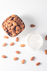 Organic almond milk in glass with raw almonds on white table 