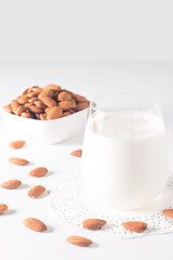 Organic almond milk in glass with raw almonds on white table 