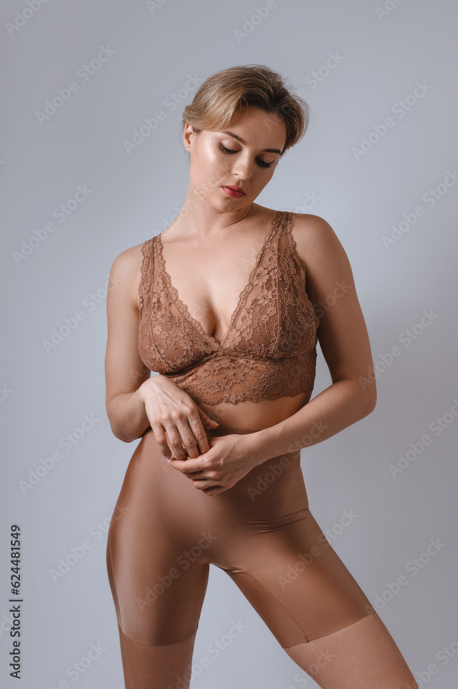 Poster portrait of young attractive woman wearing brown lace bra and high waist shaping briefs against gray