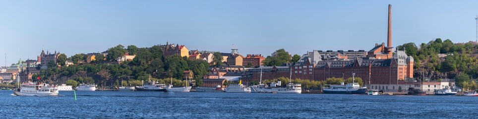 Fototapeta na wymiar Panorama, tourist steam boat and modern ferries, industrial brick buildings, , hill Maria. district Södermalm, moored old fishing and hotel boats, a sunny summer evening in Stockholm