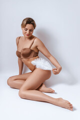 Young attractive woman wearing brown lingerie is touching her body with soft feather