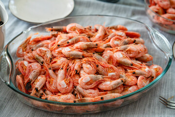 A dish of unpeeled shrimp on a dinner table with plates. Seafood diner. Boiled shrimps. vegetarian dinner, food.