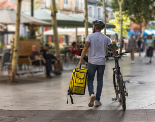 adult worker walking with his bicycle and his backpack in his hand with the background out of focus