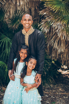 beautiful indian family father with daughters girls smiling with a bindi and traditional sari dress and kurta in front of palm fronds