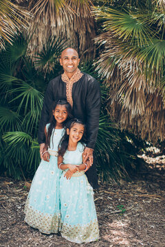 beautiful indian family father with daughters girls smiling with a bindi and traditional sari dress and kurta in front of palm fronds