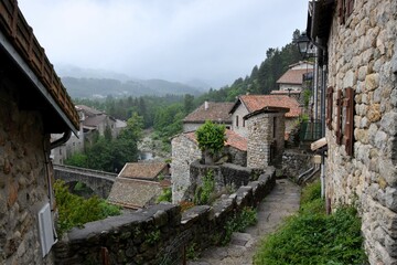 Fototapeta na wymiar Jaujac village in Ardeche, Massif Central, France, in the rain without people - dark, volcanic stone and flowing river under ancient stone bridge