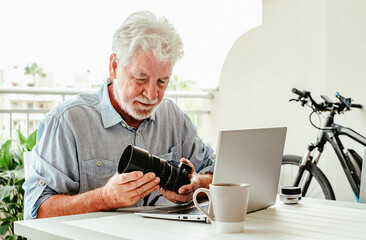 Smiling senior white haired photographer sitting outdoor on terrace holding his camera, elderly man doing business from home using online technology