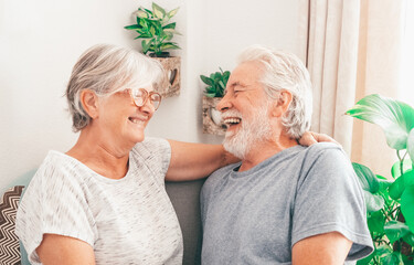 Portrait of cheerful white-haired senior family couple laughing sitting at home.  Happy elderly man and woman embracing having fun together