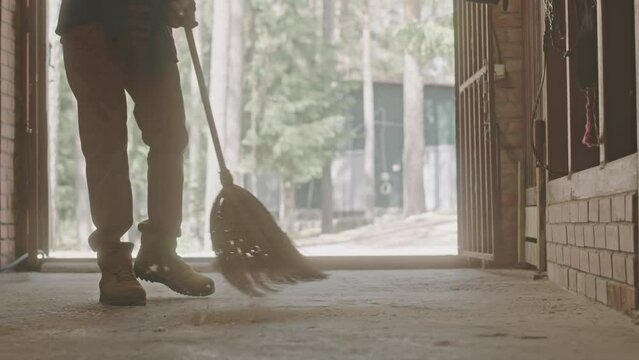 Cropped low section shot of legs of farm worker sweeping floor in horse stable