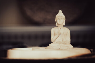 Small sunlit Buddha statue in front of a brown background