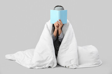 Beautiful young woman with soft blanket reading book on grey background