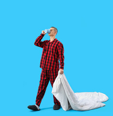 Young man with blanket drinking coffee on blue background