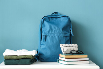 Table with stack of stylish school uniform, backpack, books, eyeglasses and pencil case near blue wall in room, closeup