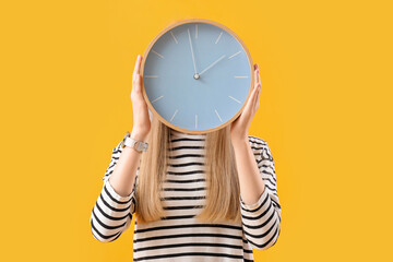 Young woman with clock on yellow background. Deadline concept