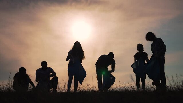 Teamwork.Silhouette of group of people clean up garbage at sunset in nature.Environmental pollution.Family cleaning plastic garbage in bag.People volunteers cleaning garbage in nature in summer park