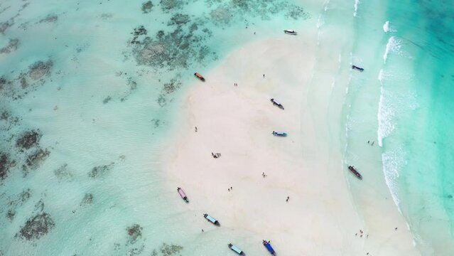 4K flying drone footage of boats on white sandbank coast with beautiful transparent rippled waves washing coral reefs atoll. Mnemba island, Zanzibar, Tanzania.Traveling in innocent Nature concept.