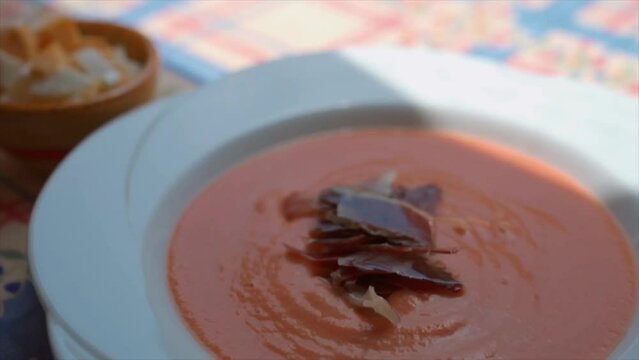 Woman garnishing Salmorejo with jam&oacute;n  as a finishing touch